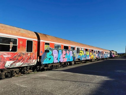 Long train with colorful graffiti on rails, blue sky above, former German railway, Shkodra, Albania