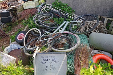 Old bikes and various objects lie messy in a garden with a warning sign, scrap collection, St