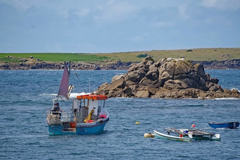 A small fishing boat out at sea off a rocky coast with colorful sails and clear skies, St Agnes,