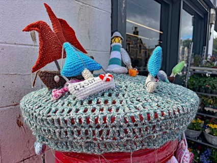 Colourful crocheted motifs of ships and houses on a wall in a maritime scene placed on a letterbox,