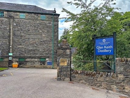 Entrance to Glen Keith Distillery with stone buildings and signs in a wooded area, Keith,