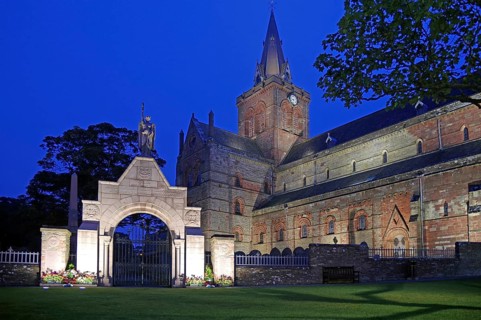 Illuminated historic church with clock tower and memorial in the evening, St Magnus Cathedral,