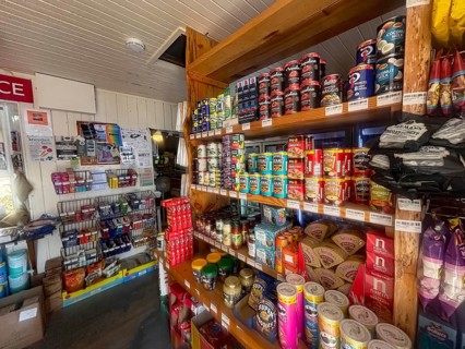 A small shop with stocked shelves full of cans and colorful food products, the only shop in the