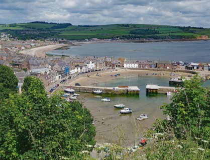Coastal view of a village with harbour, boats and green hills under a cloudy sky, Stoneheaven,