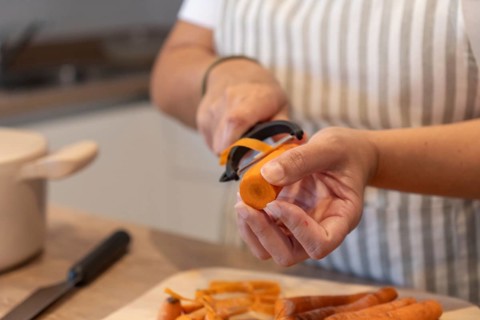 Close up of hands peeling fresh carrot in home kitchen. Healthy ingredients, simple food