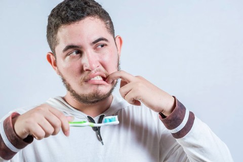 Young man with tooth sensitivity holding a toothbrush isolated. Man suffering from gum pain holding