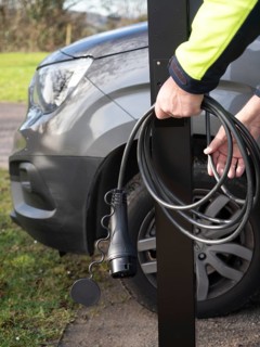 Worker holding ev charging cable next to vehicle, preparing for installation
