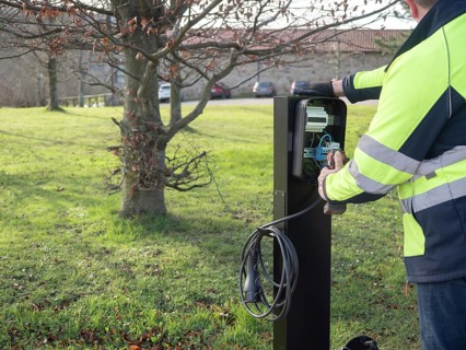 Worker installing electric vehicle charging station, connecting wires in the open panel