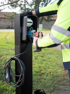 Worker installing an ev charging point, connecting wires and using a power tool for sustainable