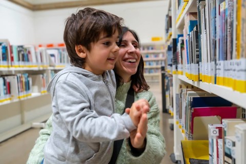 Happy mother and son enjoying a moment of discovery and learning while looking for books on shelves