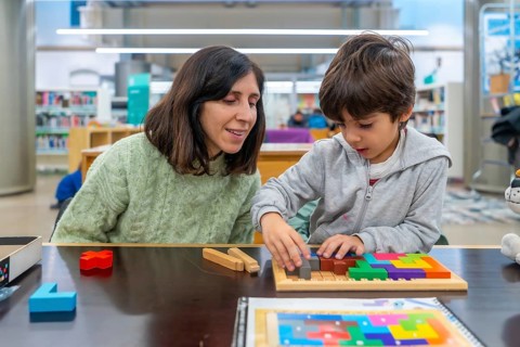 Woman and boy are playing with a colorful wooden tangram puzzle, focusing on solving the geometric