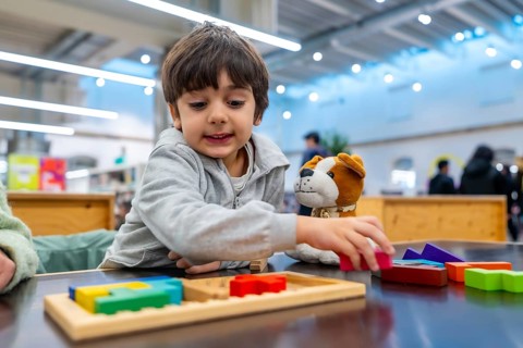 Young boy concentrating as he arranges colorful wooden puzzle pieces beside a soft toy dog,