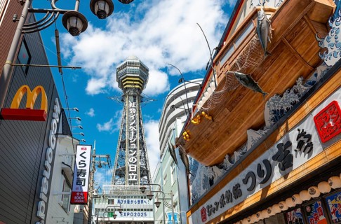 Lots of colorful signs in a pedestrian zone with shops and restaurants, behind Tsutenkaku Tower,
