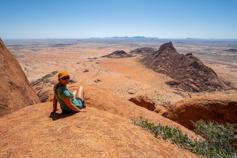 Woman sitting on rocks and enjoying the view over the barren desert landscape of Spitzkoppe,