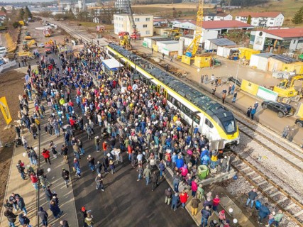 Many people at an event with train and construction site near a train station, opening of the