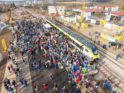 Large crowd at an event with train and cranes on a construction site, opening of the Hermann Hesse