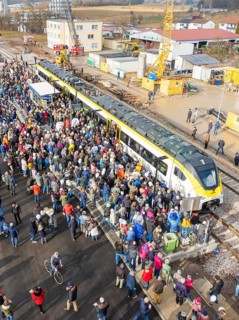 Many people gather at an event near a construction site by train at a train station, opening of the