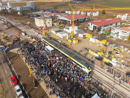People gather around a train on a construction site, aerial view with landscape in the background,