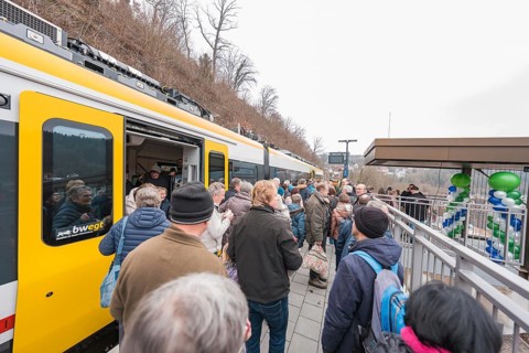People standing on a platform next to a decorated train, platformside celebration, opening of the