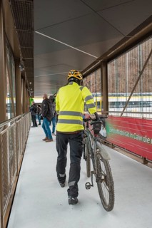 Cyclist wearing yellow safety clothing pushes a bicycle across a modern bridge, opening of the