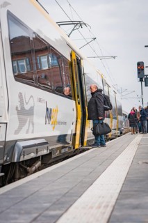 People board a train at a train station with a cool, cloudy atmosphere, opening of the Hermann