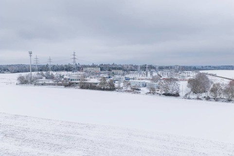 A wide snowy field with power lines and a substation in the distance, substation, Jettingen,