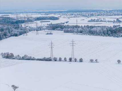 Wide snow-covered fields with power lines and small villages on the horizon in cold weather,