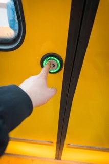 Close-up of a hand pressing a green door button on a yellow train, battery electric train Siemens