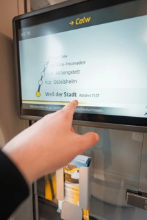 Hand points at a display with timetable and departure times on the train, battery electric train