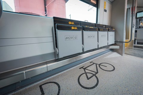 Train compartment with marked bicycle parking spaces and grey folding seats, battery electric train