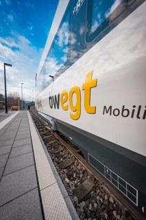 View along the rail of a white-blue train with MOVING branding under a blue sky, Siemens Micro Plus