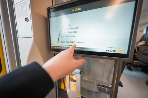 Display screen with timetable and hand showing departure time, battery electric train Siemens Micro