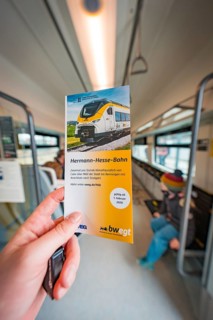 Hand holding brochure about the Hermann-Hesse railway inside the train, battery electric train