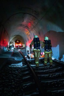 Firefighters walk on tracks through a dark tunnel with red light effects, fire drill on the Hermann