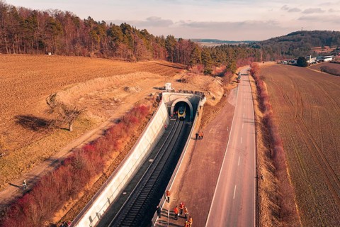 Aerial view of a railway tunnel next to a road and emergency services surrounded by trees, fire