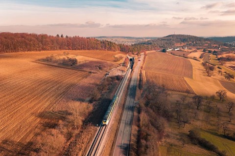 Wide landscape with railroad tracks and a distant train, surrounded by fields and forests, fire