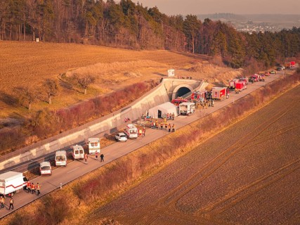 Emergency vehicles with firefighters near a tunnel next to fields and trees at dusk, fire drill on