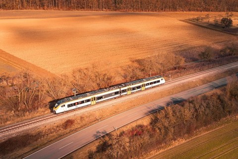 Train travels along railroad tracks between fields and forest at sunset, fire drill on the
