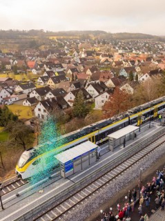Train stops at a train station in a small town with many spectators and houses in the background,