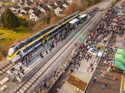 Large groups of people receive a train on the platform, surrounded by city and nature, opening of