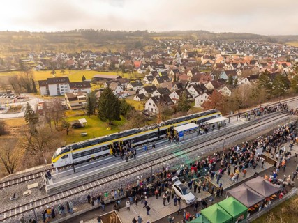 Train stops at a platform in a small town surrounded by people and houses, opening of the Hermann