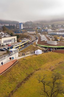 A large crowd gathers at a station area in a hilly landscape, opening of the Hermann Hesse Railway,