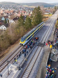 A train stops at a platform surrounded by a crowd of people. In the background you can see a