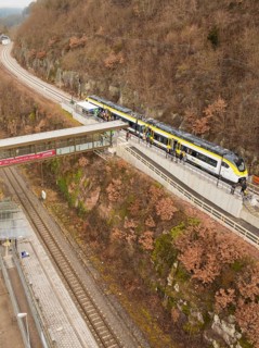 A train stops at an elevated station in a hilly autumn landscape, opening of the Hermann Hesse