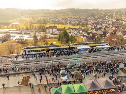 Numerous people at a village train station, festive atmosphere upon arrival by train, opening of