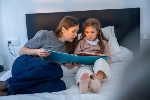 Mother and young daughter share a quiet bedtime moment reading together in bed, fostering