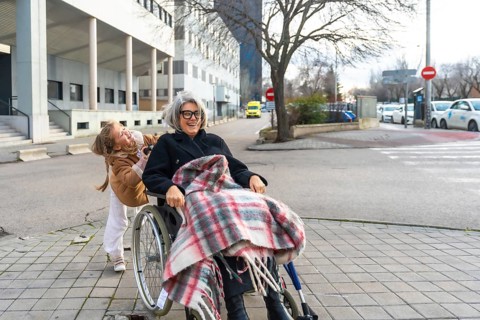 Granddaughter joyfully pushing her smiling grandmother in a wheelchair, exploring the city together