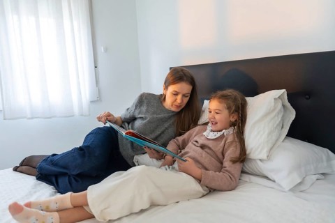 Mother and young daughter bonding over a book in bed, sharing a laugh and enjoying quality time