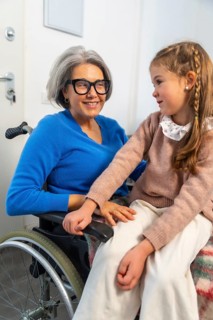 Granddaughter tenderly interacting with her smiling grandmother in a wheelchair, symbolizing strong