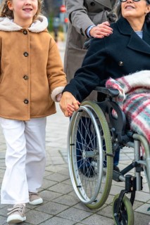 Granddaughter walking alongside her grandmother in a wheelchair, holding hands, with a woman